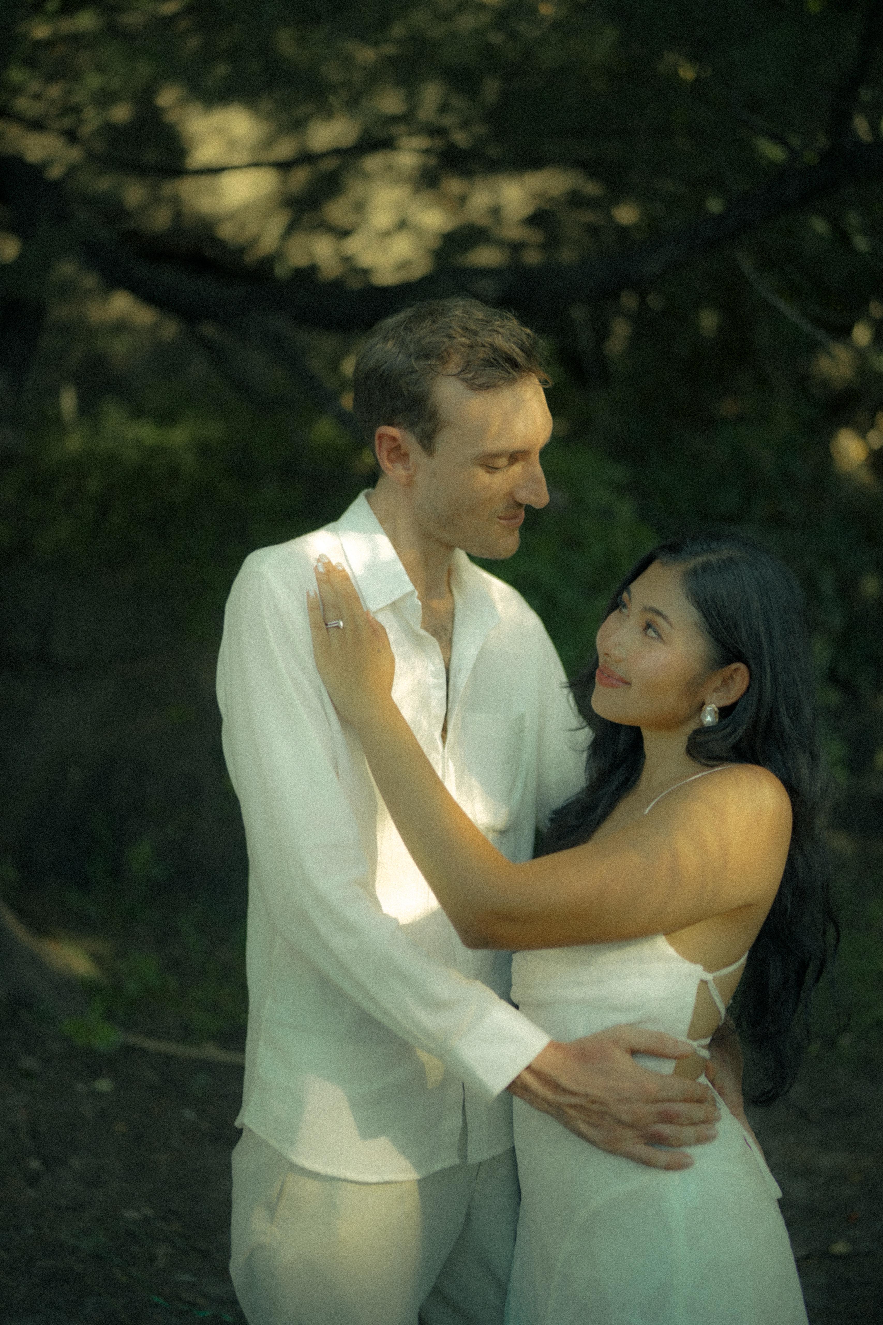 Carlo and Jai Jai in a tender embrace under a leafy canopy at golden hour