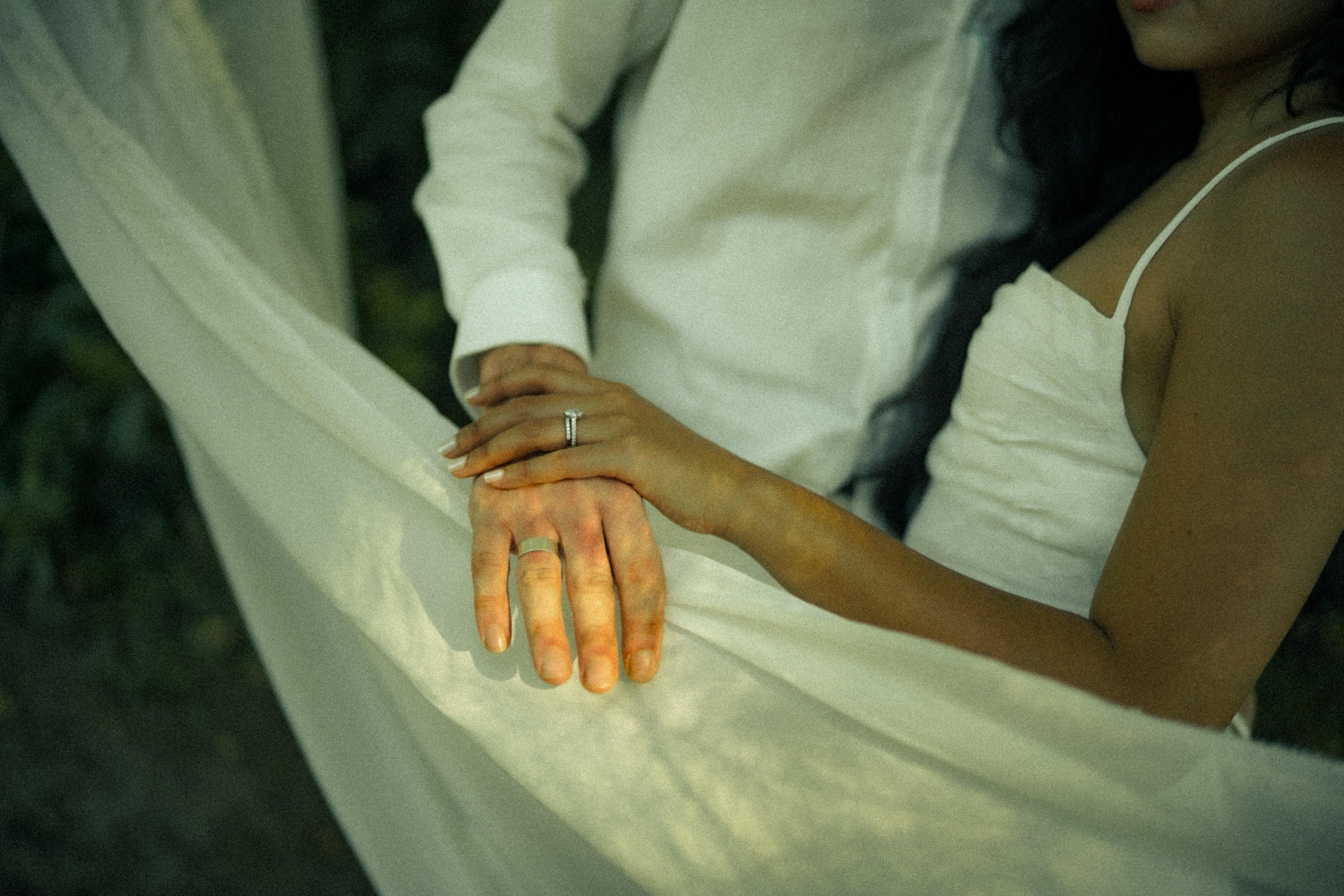 Detail of clasped hands resting on a flowing white veil with the engagement ring visible