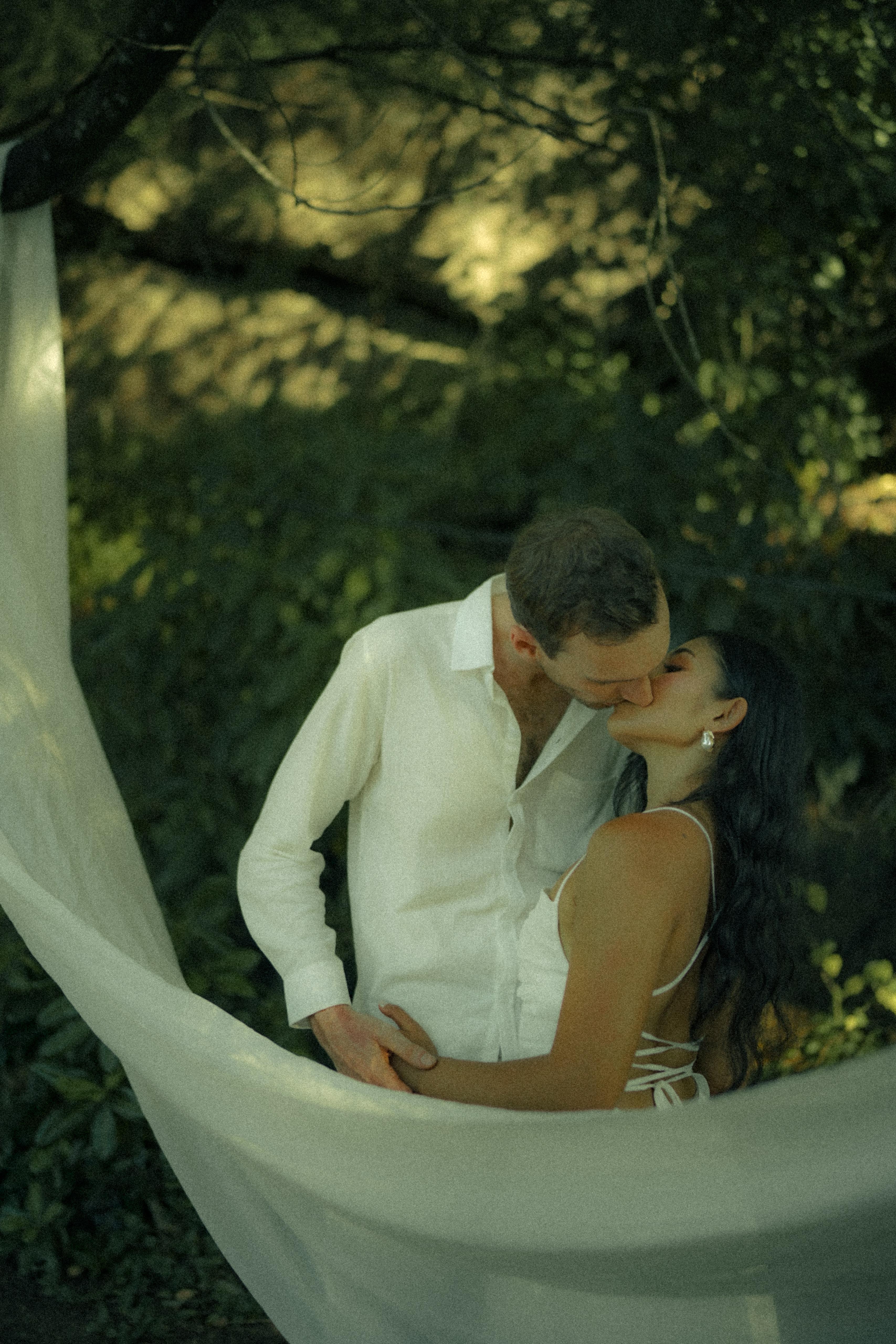 Carlo and Jai Jai sharing a kiss inside a white veil swing in the garden