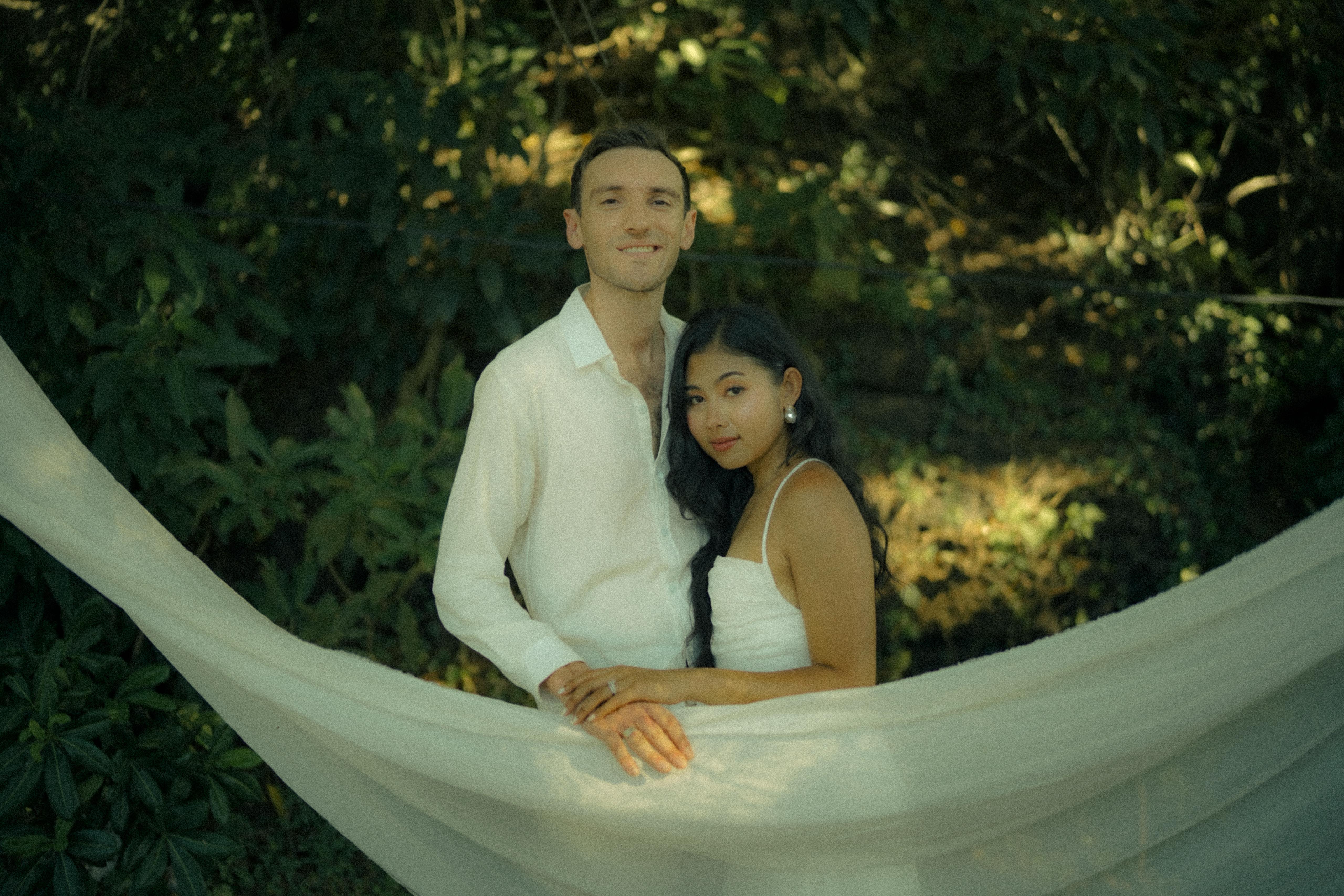 Carlo and Jai Jai together inside the white veil swing, lush greenery behind them